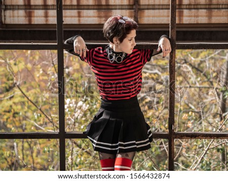 Goth punk girl portrait with a skirt and striped stockings chilling out on rusty metal structures in an abandoned factory. A young generation of alternative teens concept