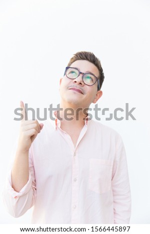 Positive guy in eyewear pointing finger up. Young man in glasses standing isolated over white background. Presenting or advertising concept