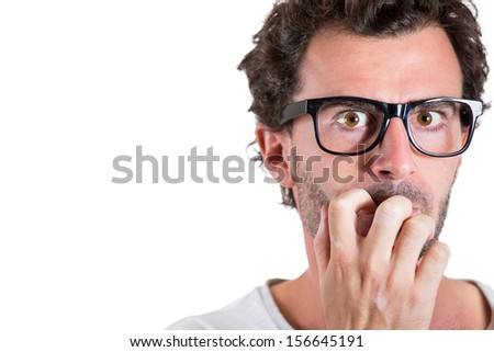 Closeup portrait of a nerdy young guy with glasses biting his nails and looking at you with a craving for something or anxious, isolated on white background. Human facial expressions.