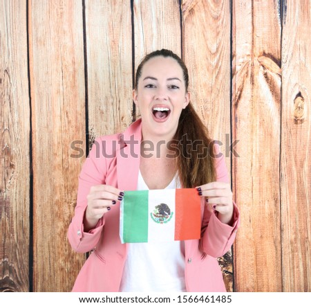 Excited young business woman holding a flag of Mexico against a wooden background