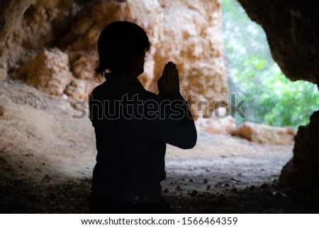 Silhouette of a young man praying inside a cave at the woods in Mallorca, Spain