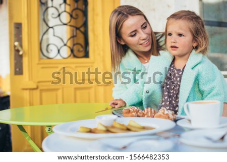 Family picture of young woman and child together in restaurant. Sit and spend time together. Pancakes and cup of coffee on table. Mother and daughter