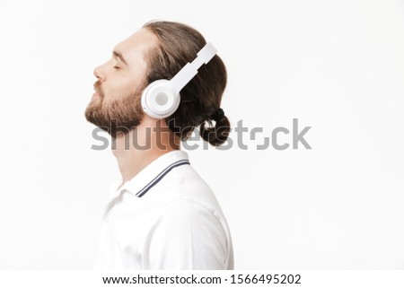 Photo of a young handsome bearded man posing isolated over white wall background listening music with headphones.