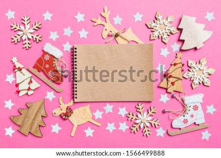 Top view of notebook, pink background decorated with festive toys and Christmas symbols reindeers and New Year trees. Holiday concept.