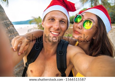 Happy couple in Santa's hats having fun and sits at tropical beach. New year beach holidays concept