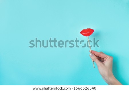 Hand holding Red Lips Lollipop. Lollipop candy in the shape of red lips, minimal concept composition on blue background, copy space.