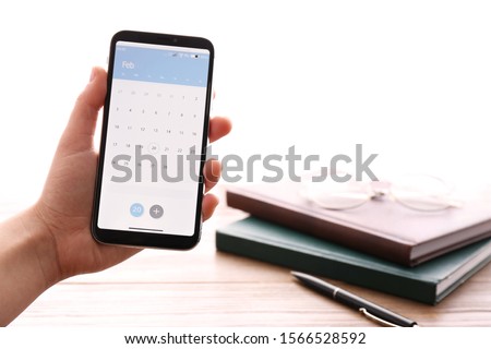 Woman holding smartphone with calendar app above table, closeup