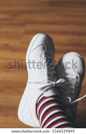 A vertical shot of a person's feet wearing white shoes and striped red, blue and white socks