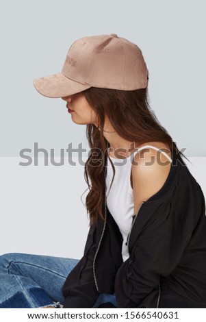 Cropped side photo of a girl, wearing beige velvet baseball cap with embroidery lettering "patience", white tank top, black jacket and jeans with scuffs.  Girl has large hoop earrings. 