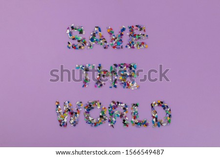 Recycled save the world text consisting of small plastic pellets collected from the sea water. Rethinking the environment by reducing or reusing plastics. Circular economy concept. Purple background