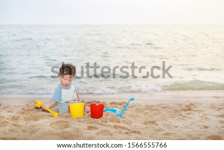 Adorable little Asian baby boy playing sand at beach.