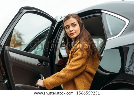 Young woman getting out of taxi and looking away