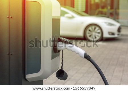 EV Car or Electric car at charging station with the power cable supply plugged in on blurred city background