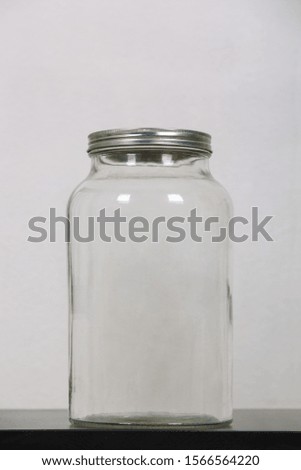 Close up photo of an empty jar, on the table, closed with a metal lid isolated over grey background with copy space. Glass bottle package for canning and preserving