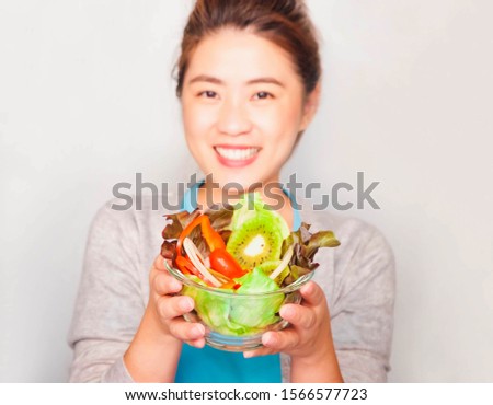 Young beautiful asian woman wore blue t-shirt and gray coat, holding a clear glass cup with salad vegetables,Bright smile health care Eat vegetarian food,Selective focus