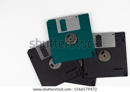 Four old floppy disks in a heap lie on a table with a white background. The color of one diskette is green.