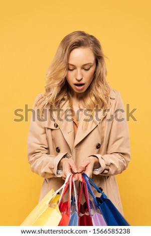 Surprised woman holding shopping bags isolated on yellow