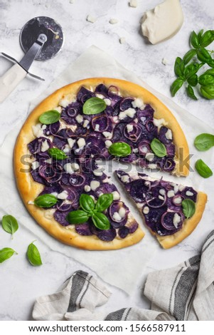 Pizza with purple potatoes, red onions, goat cheese and basil on a marble table. Sliced slice of pizza. Top view 