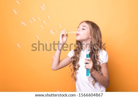 young girl blowing soap bubbles on an orange background. time to have fun