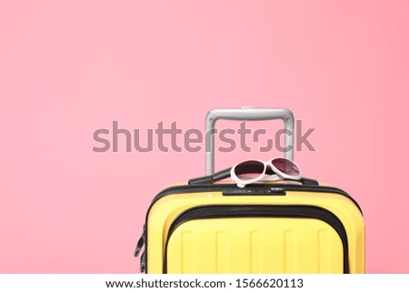 Yellow suitcase with sunglasses on pink background. Space for text