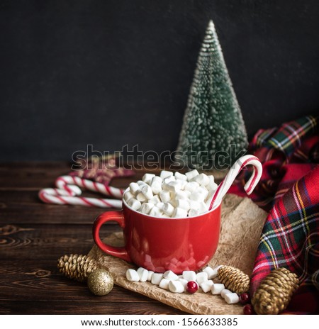 Cappuccino with marshmallow in red mugs and  striped stick candys, fir cones on wooden table. Christmas holiday mood concept. Cozy Winter background