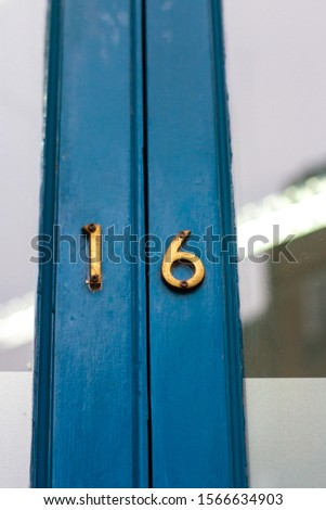 House number 16 with the sixteen in bronze metal digits on a blue wooden front door with glass panels