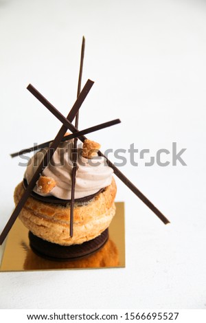 Choux (profiteroles) with chocolate creme, salted caramel, and whipped ganache with milk chocolate, and chocolate decor. Choux is on a golden cardboard cake base, on a white background.