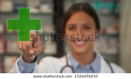 Portrait of an young female pharmacist consultant is smiling in camera and touching a pharmacy icon in a drug store.