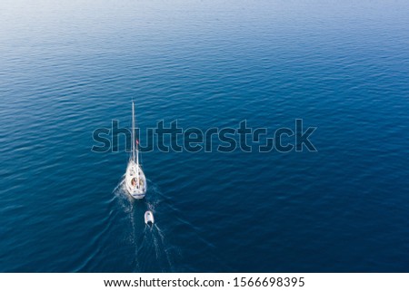Motor-sailing mini yacht with a rescue boat tied to it floats on the sea. The view from the top.