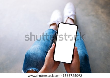 Top view mockup image of a woman holding black mobile phone with blank white screen while sitting on the floor