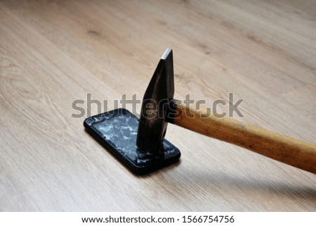 Broken mobile phone screen with a big black iron hammer. LCD screen broken, cracked and unusable smart phone. Hammer Smashing Cellular Phone.