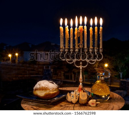 Sweet donut, festive burning candles, jar of olive oil and dreidels with four-sided spinning top. Each side of the dreidel bears Hebrew letter that together translated as - a great miracle happened he