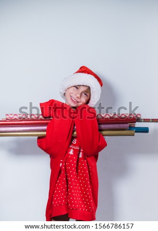 Charming boy wearing Santa's Hat red sweater prepared to packing Christmas gifts and boxes into brightnes vintage wrapping paper Concept fun preparation to holidays