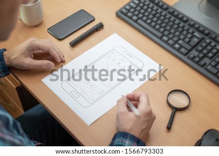 The designer sketches, draws the layout of a mobile phone app on a wireframe.
