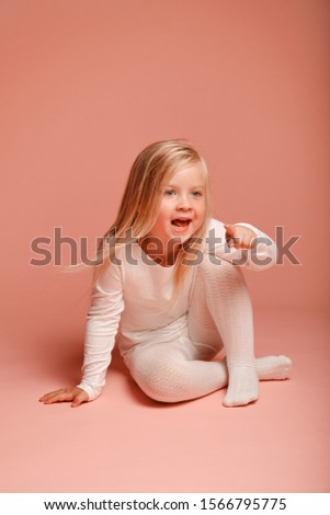 Cute little girl sitting on the floor on a pink background in the studio. Kindergarten, childhood, fun, family concept. fashion baby