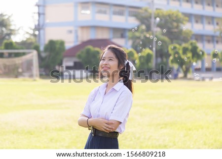 Asian cute girl in a white school uniform is playing a bubble balloon on the lawn. Cute girl is playing soap bubbles in the garden.
