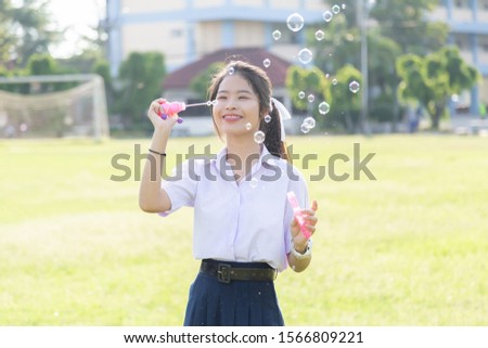 Asian cute girl in a white school uniform is playing a bubble balloon on the lawn. Cute girl is playing soap bubbles in the garden.