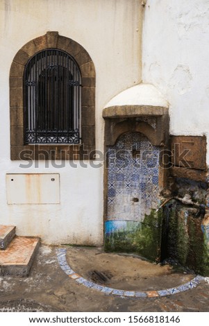 White walls of a house with a window with an arc. Well decored by traditional tiles in the corner. Old city (medina) of Essaouira, Morocco.