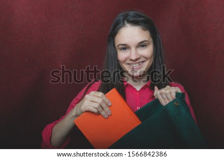 photo of a young beautiful girl with dark hair; a young girl holding a book of books and a green backpack; studio photography
