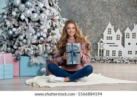 Beautiful girl in pink sweater with christmas box gift near pink and blue Christmas tree. Magical time.
