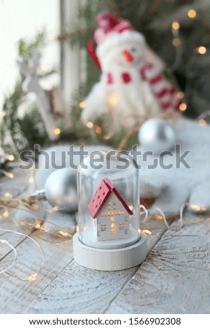 Toy snowman, house, Christmas decor, illumination on a wooden surface on a background of a window, decorating the interior for winter seasonal holidays
