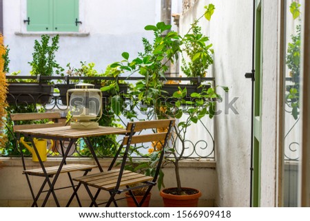 An Italian balcony with green potted plants and garden furniture. a table and chairs to enjoy the balmy evening. Royalty-Free Stock Photo #1566909418