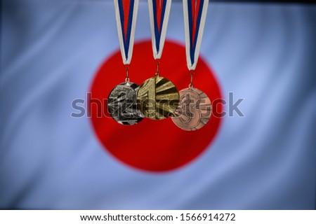 Silhouette of tree medal: Gold, Silver an Bronze. Japan flag in background.