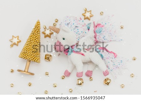 knitted flying unicorn on a white background with a Christmas tree and golden stars