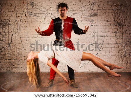 Magic moment - man in medieval suit performing magically levitating his girl assistant