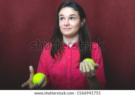 photo of a young girl with dark hair; picture of a girl with tennis balls; studio photo of a young girl on a red background
