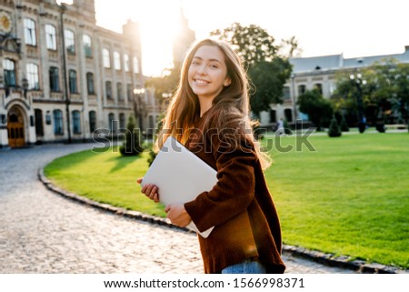 Charming young woman student in move walking in university garden with laptop computer, going to her classroom, beautiful sunset background, positive emotions, lifestyle people