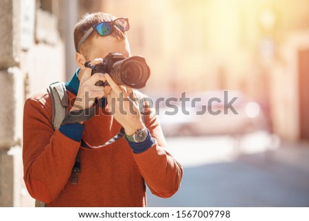 Portrait happy male traveler photographer holding camera in hands, blurred background.