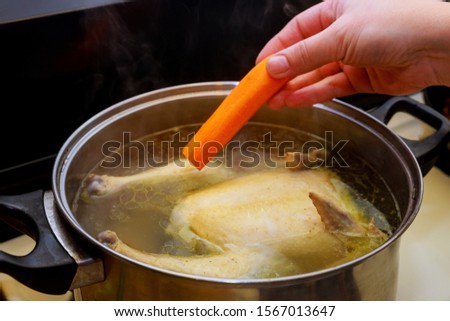 Womens hand puts carrot in the chicken broth in the pot.