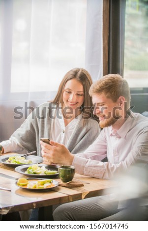key opinion leader millennial woman or girl makes selfie on smartphone camera to share on internet social media channels.couple in a cafe smiling looking at the phone